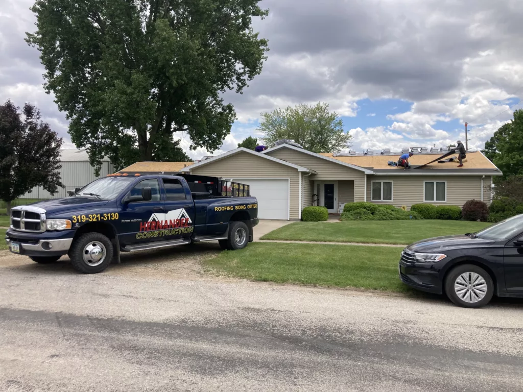 Hernandez KD Construction truck in the driveway with the roofing crew on removing asphalt shingles on a home in Stanwood, Iowa