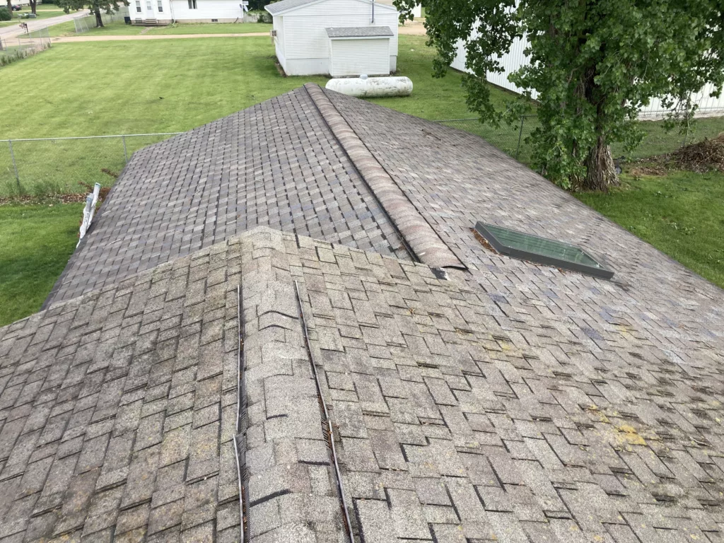 Original roof with missing asphalt shingles due to wind and hail damage roof in Stanwood, Iowa. With skylight.